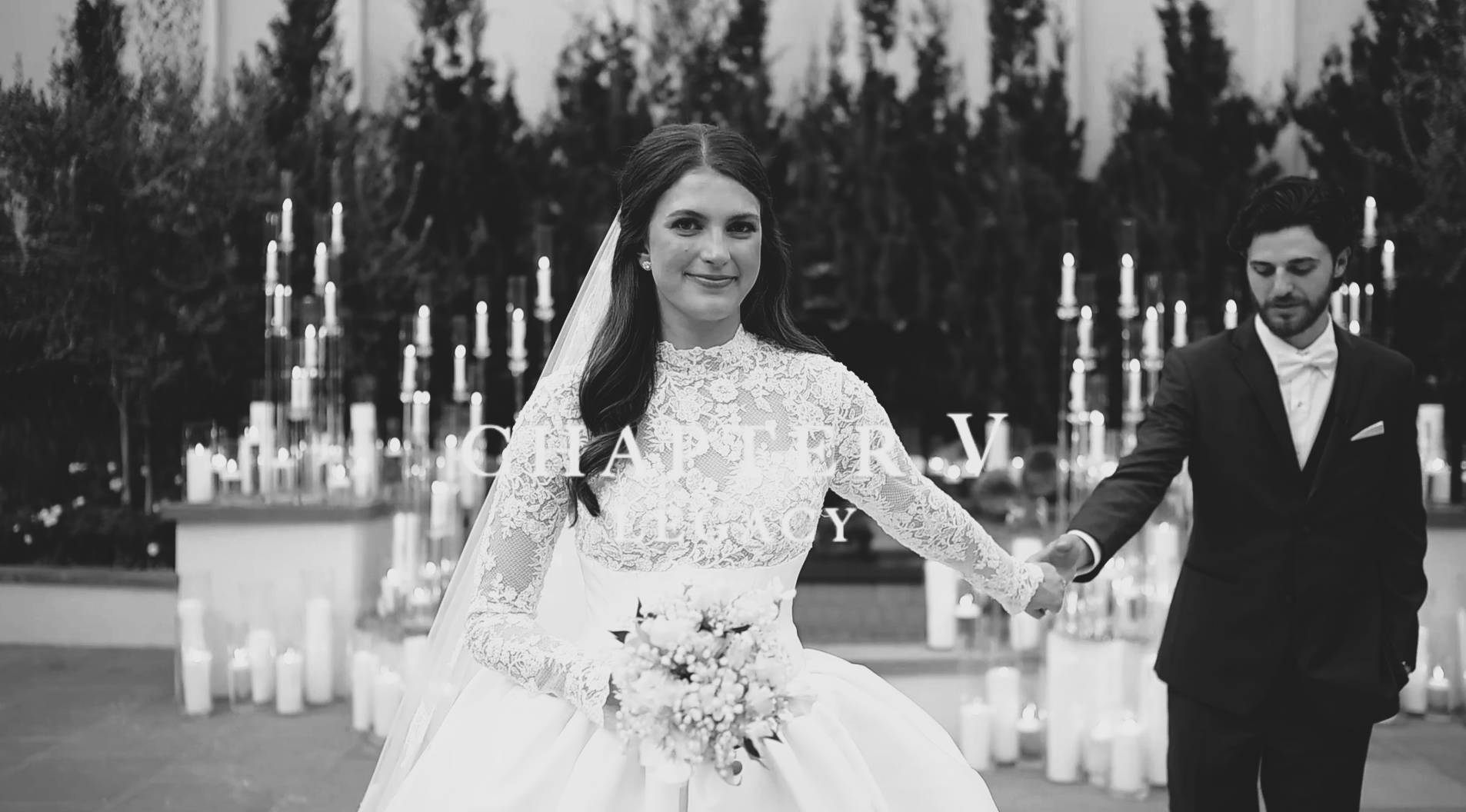 Bride holding grooms' hand in front of candles.