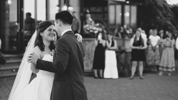 A bride and groom dance while family and friends watch in the background.