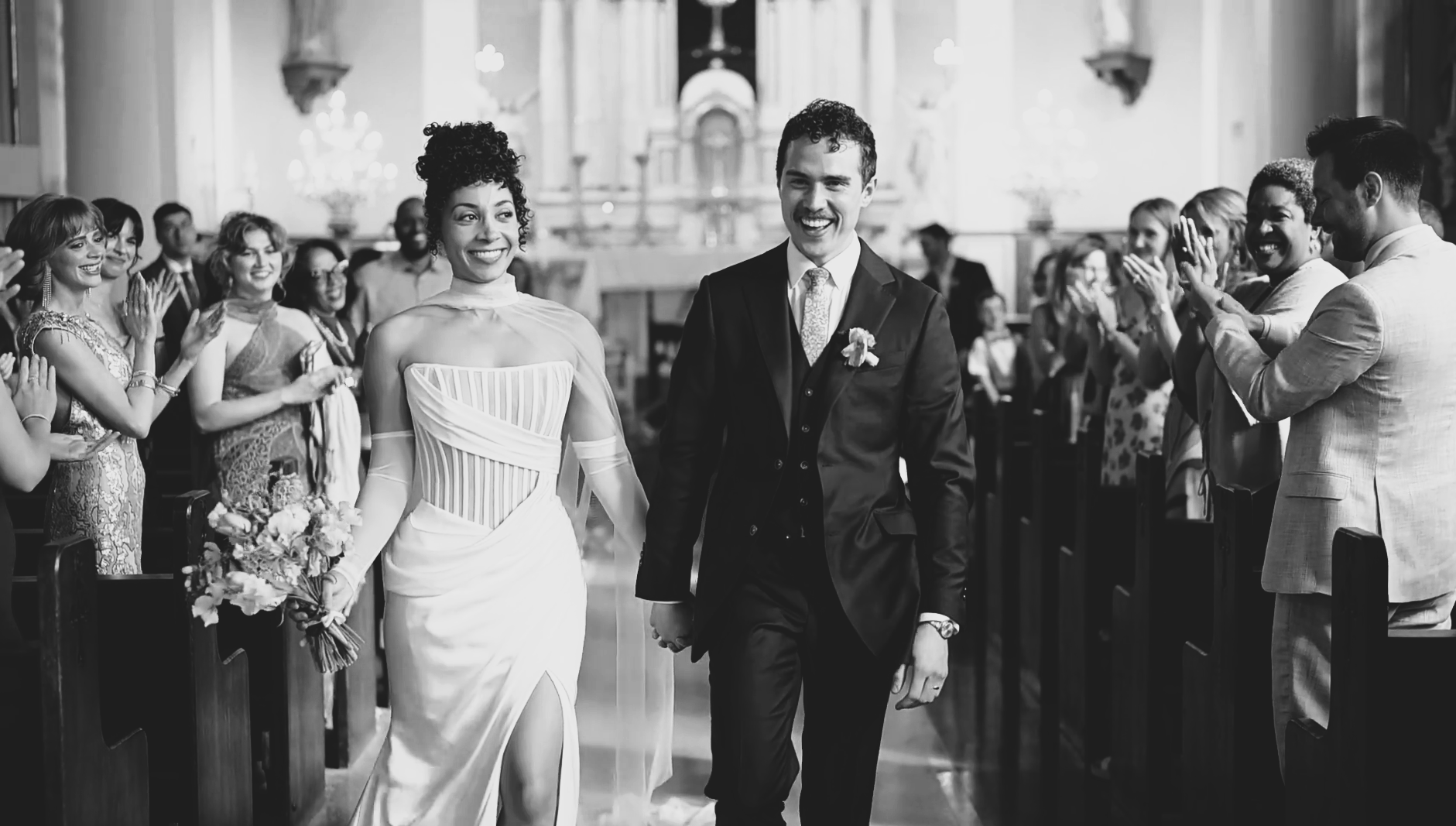 A happy bride and groom walk down the aisle of a cathedral after getting married. Happy friends and family applaud.